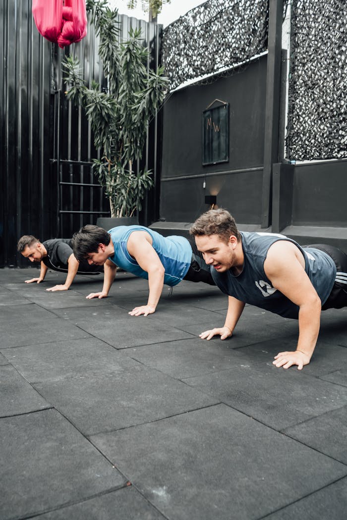 Three adult men doing push-ups outdoors in Mexico City gym.