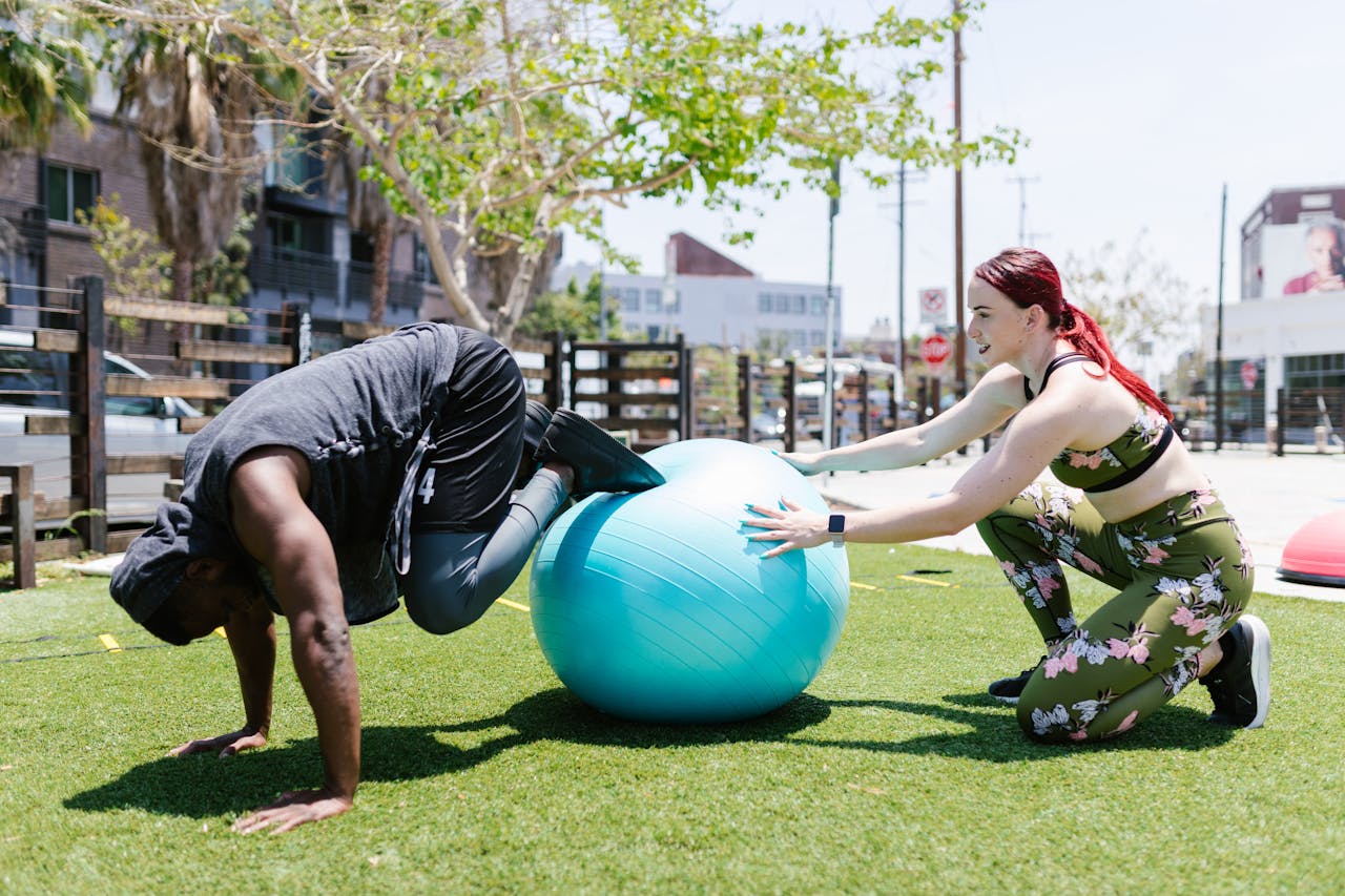 Two people performing a joint fitness workout with a fit ball outdoors.