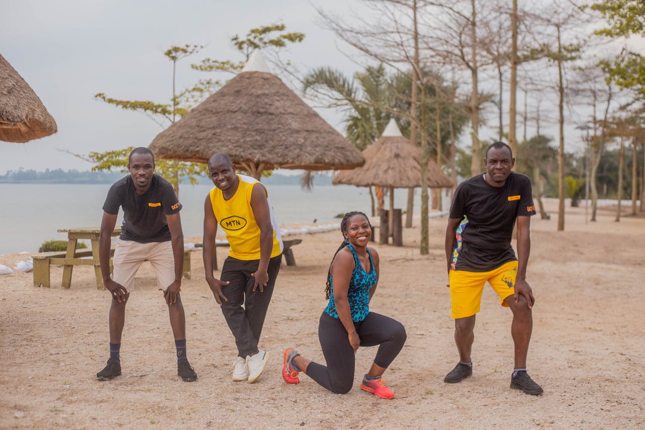 Four friends enjoying a workout session on a sandy beach with huts.